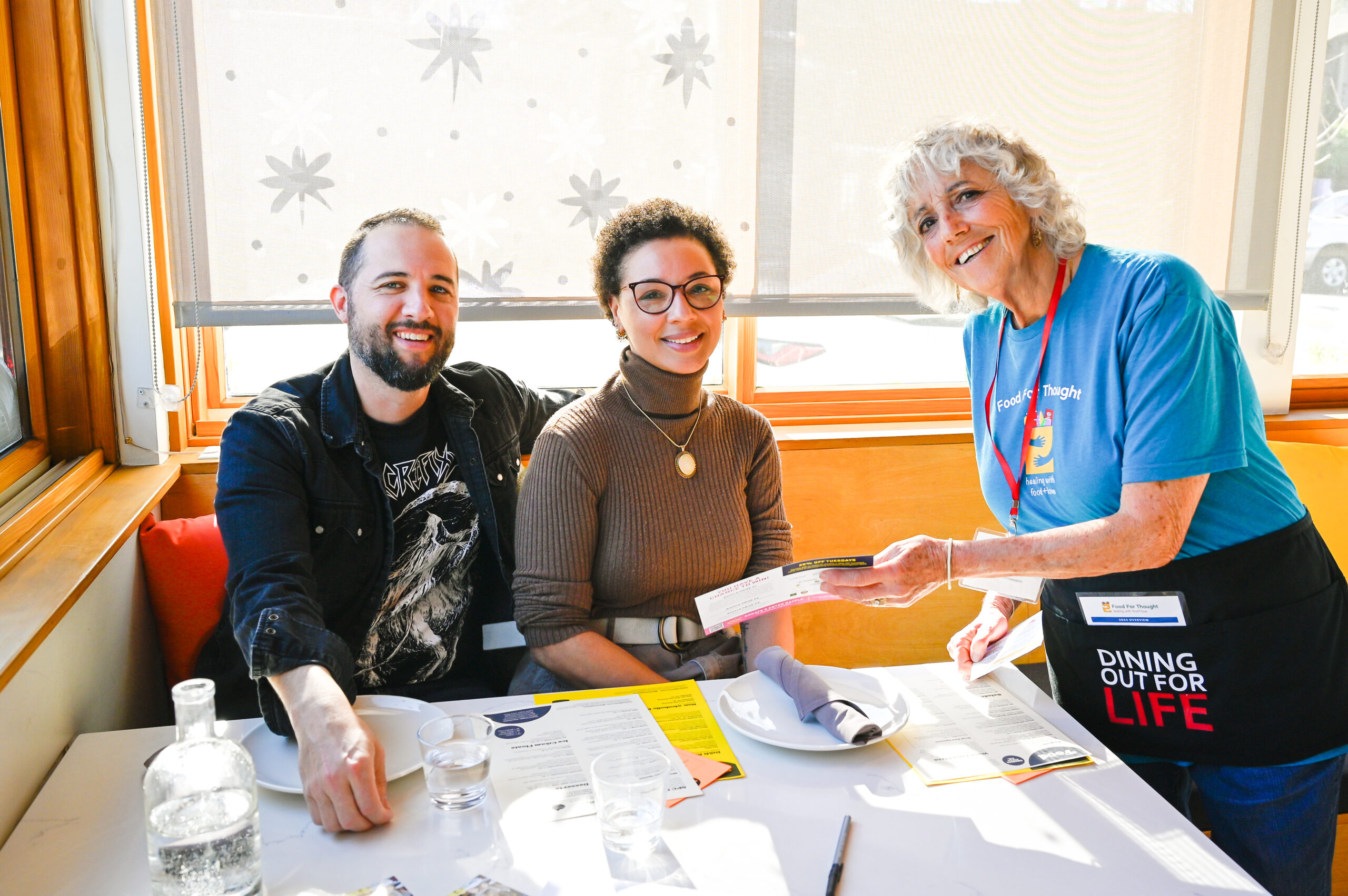 Dining Out For Life volunteer handing Food For Thought information to happy diners