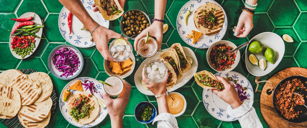 A table full of food and hands holding drinks cheersing
