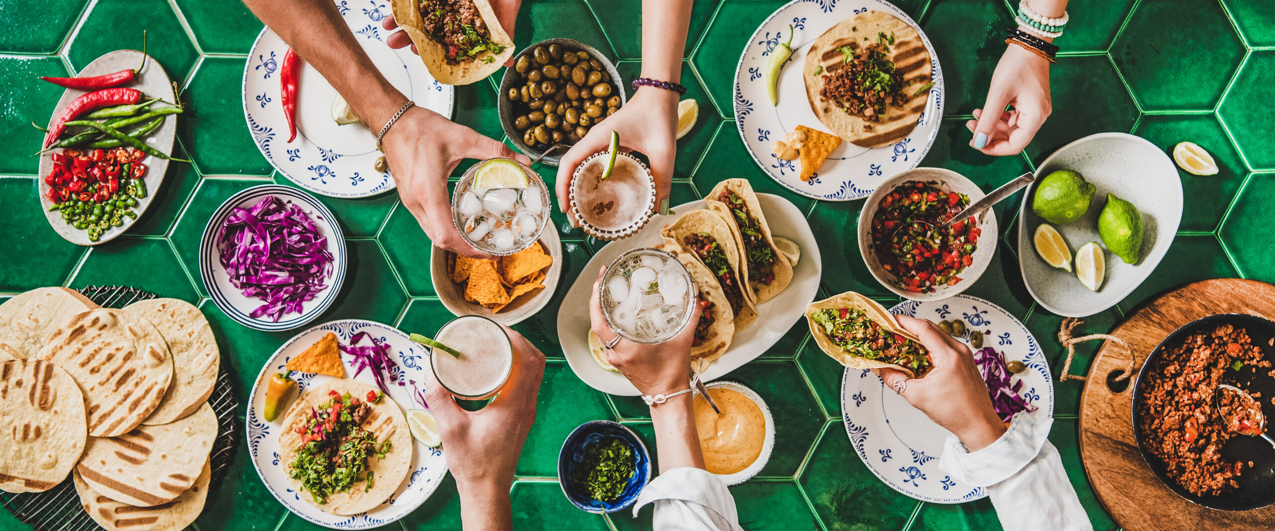 A table full of food and hands holding drinks cheersing